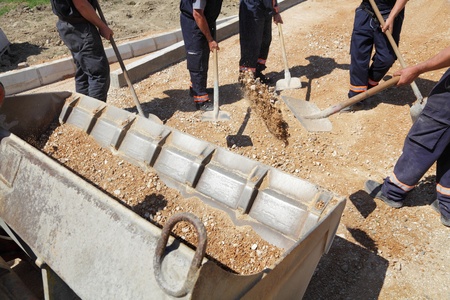 Workers team throw gravel into bulldozer bucket with shovels の写真素材