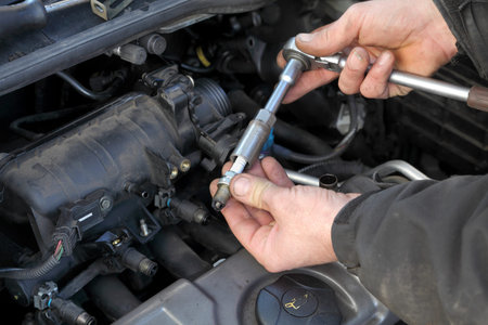 Modern car gasoline engine servicing, workers hands, ratchet and spark plug