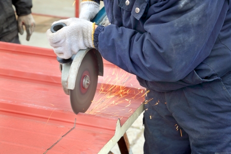 Cutting of heat insulated galvanized corrugated sandwich roof panel, workers hands angle grinder toolの写真素材