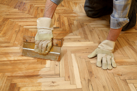 Varnishing of oak parquet floor, workers hand and toolの写真素材