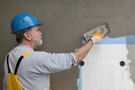 Worker spreading  mortar over styrofoam insulation and mesh  with trowelの写真素材