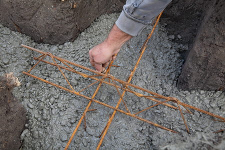 Worker placing reinforcement to concrete in wall foundation at construction siteの写真素材
