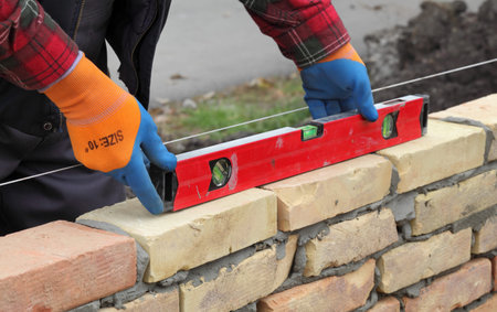 Worker control brick wall using level tool, selective focus, real people