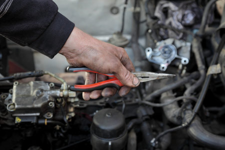 Dirty mechanic hand  hold long nose pliers in hand with car engine in background