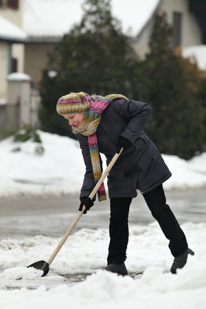 Caucasian woman cleaning snow from sidewalk at street using shovel, winter timeの写真素材