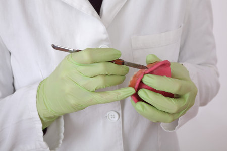 Dentist modeling wax prothesis model using dental modeling knife, closeup of hands in gloves and...