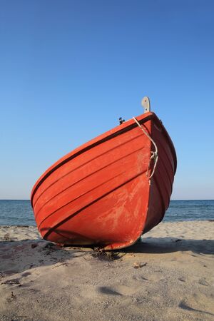 Old red boat at sand on beach with clear blue skyの写真素材