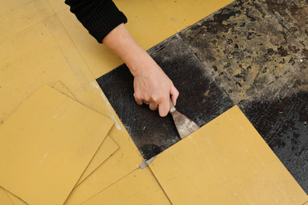 Worker removing old vinyl tiles from kitchen floor using spatula trowel tool
