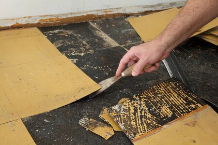 Worker removing old vinyl tiles from kitchen floor using spatula trowel toolの写真素材
