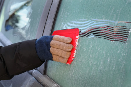 Winter scene, human hand in glove scraping frozen ice from window of car