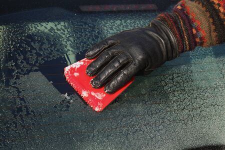 Winter scene, human hand in glove scraping frozen ice from windshield of carの写真素材