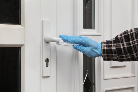 Human hand in protective gloves  cleaning house door handle using antibacterial or cleaning solution and wet wipesの写真素材