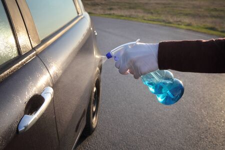 Young driver with protective gloves spraying antibacterial or cleaning solution from sprayer bottle to handle of car doorの写真素材