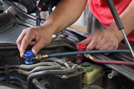 Mechanic charging air condition unit at modern car, closeup of workers hands and equipment conected to car engine, red and blue clucth couplingsの写真素材