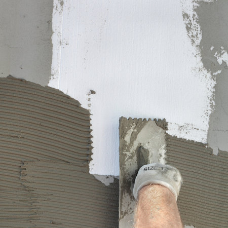 Workers hand spreading  mortar over    polystyrene insulation and netting using trowelの写真素材