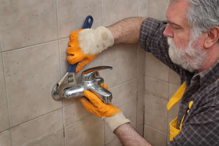 Plumber fixing or replacing old faucet in a bathroom, closeup of hand in glove, tap and adjustable wrench toolの写真素材