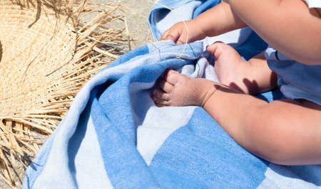 Baby feet. The kid is sitting on a beach towel. Straw hat and sand. Carefree childhood.の写真素材