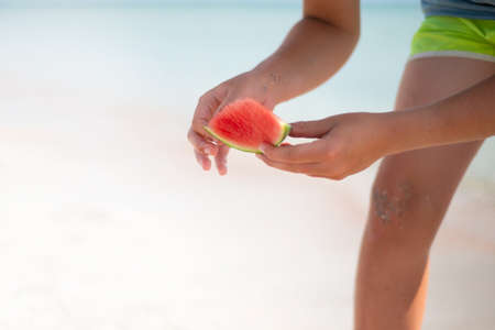 A slice of watermelon in the hands of a teenager. Eat watermelon on the beach.の写真素材