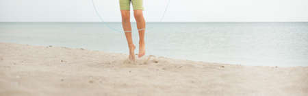 A boy on a sandy beach is jumping rope. Legs close up. Sports activities by the sea. healthy lifestyle.の写真素材