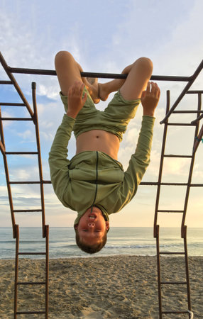 Sports equipment on the beach. The boy vmsit on the horizontal bar upside down. Leisure outdoors on...