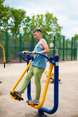 Warm up your body muscles on the simulator in the park. The teenager stands on the platform and holds on to the handles of the mechanism. sports leisure. sportsの写真素材