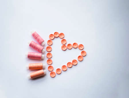 Pink spools of thread and coral buttons are lined in the shape of a heart. Needlework. Sewing. design.の写真素材