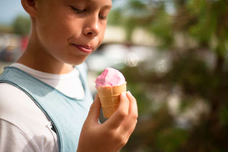 The boy holds a pink ice cream in his hand. Pleasure. positive emotions.の写真素材