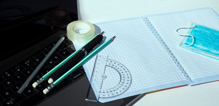 On the laptop keyboard lie a notebook pencils pens ball-point protractor adhesive tape and a...