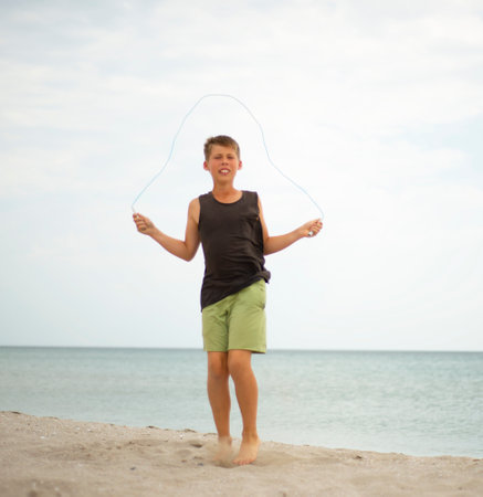 The boy is jumping rope. Sports by the sea on the sand. An effort. healthy lifestyle. workout. jumping.の写真素材