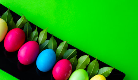 Easter. Brightly colored eggs and green young leaves on a black rectangle. Corner for text. green background.の写真素材