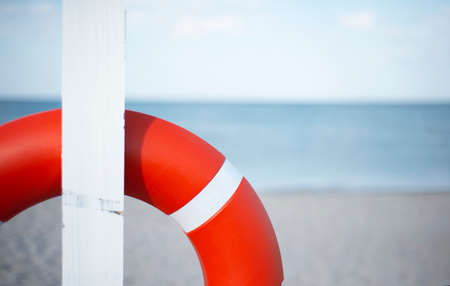 An orange lifebuoy hangs from a white post on a sandy beach. Sea horizon and copy space for text.の写真素材