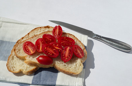 Sandwich with sliced ??cherry tomatoes on a striped napkin. Tomato slices lie on fresh wheat bread. Steel knife beside. white background.の写真素材