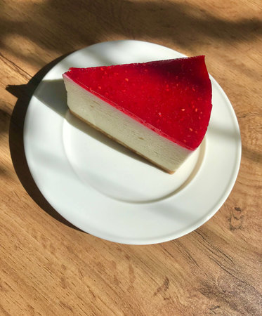 Raspberry cheesecake on a white plate. wooden table with shadows. Breakfast in a cafe.