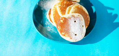 A bunch of hole pancakes with powdered sugar on a turquoise ceramic plate. Copy space on a turquoise background.の写真素材