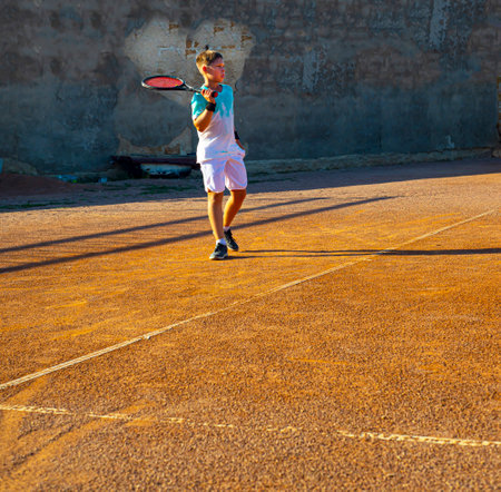 Boy teenager tennis player on a clay court. There is a heart on the wall. professional tennis training. Love for sports.の写真素材