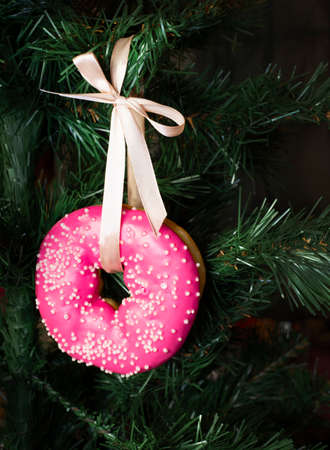 A glazed pink donut hangs from a satin ribbon on a Christmas tree. Sweet Christmas toys.の写真素材