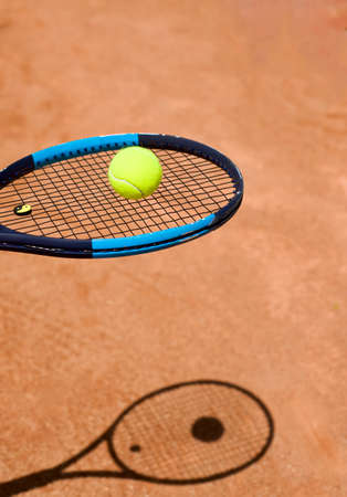 The head of a tennis racket with a yellow tennis ball. The shadow of the racket on the ground. Racket strings. Stretch. Copy space for text. sports themes. backgrounds.の写真素材