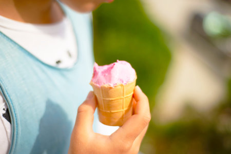 Pink ice cream in a waffle cup, bitten off and melted in the hands of a child.