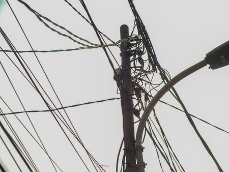 A utility pole with tangled wires and a streetlight against a bright sky.