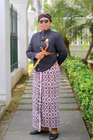 Full body portrait of an Indonesian man wearing traditional Javanese attire, holding a kris dagger,...