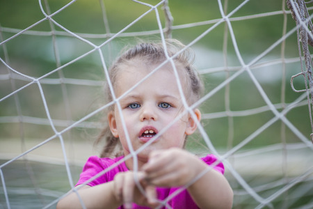 Little girl staying behind football net and playing with itの写真素材