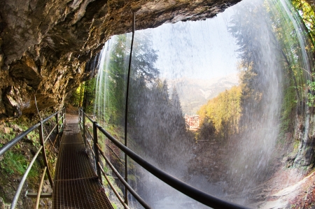 Fisheye view of a footbridge leading behind the giessbach falls at lake Brienz in the Bernese Oberland, Switzerland - the historic Grand Hotel Giessbach is visible  through the waterfall の写真素材