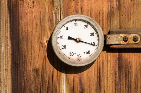 A vintage thermometer  mounted on a wooden wall in direct sunlight.