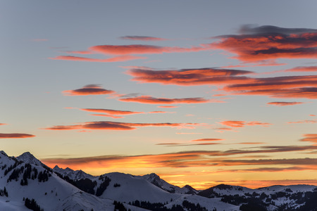 A beautiful sunset with red clouds moving over a snowy mountain range.の写真素材