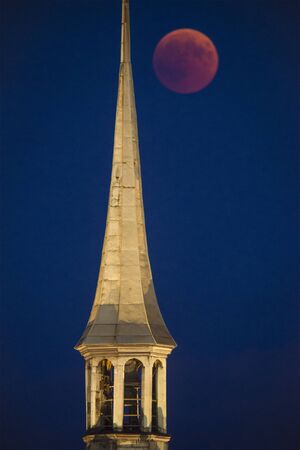 BERN, SWITZERLAND - July 27, 2018:  Total Lunar Eclipse behind the tower of Heiliggeistkirche in the Swiss Capital. Thousands of people were enjoying the spectacle on the streets in this mild summer night.の写真素材