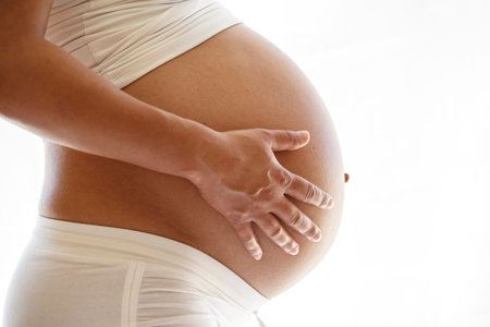 Last trimester pregnant woman holding her belly over a white background.