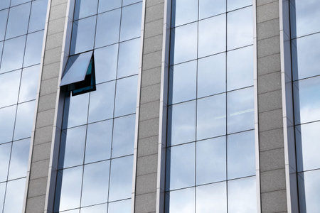 External facade of a modern glass fronted office block with one single window raised and open in a...