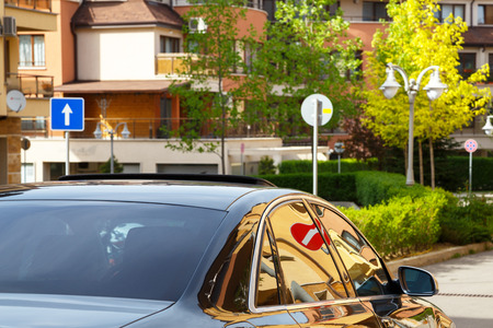 Car with dark tinted windows driving down a residential urban street with apartment blocks and multi-storey houses with a no entry sign reflected in the glassの写真素材