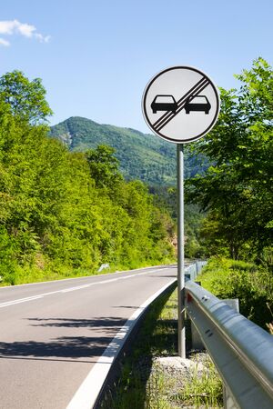 End of overtaking prohibition road traffic sign on a signpost at the side of an empty mountainous roadの写真素材