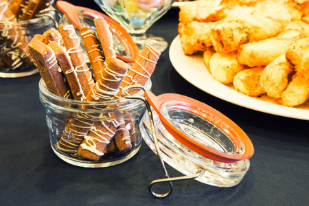Delicious dessert fingers drizzled with frosting and displayed in a glass jar besides other tasty...